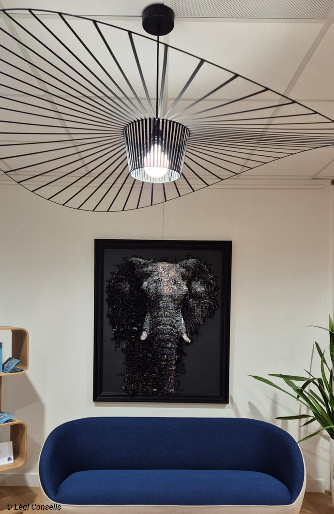 Espace d’attente avec canapé design bleu, suspension graphique et tableau représentant un éléphant, dans les bureaux de Légi Conseils.